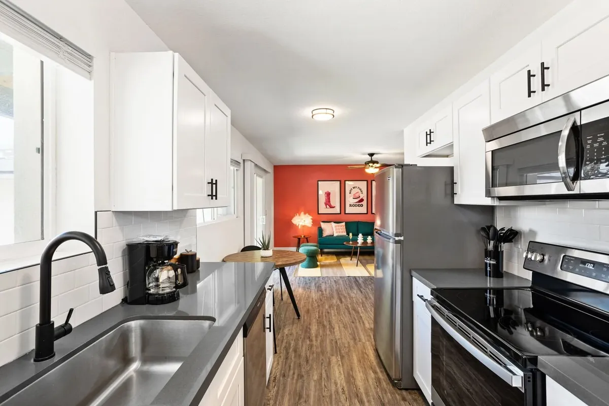 This image features an open-plan kitchen and living area with a kitchen sink, stainless steel appliances, a dining table, a green couch, and a vibrant red accent wall. The layout is spacious and inviting, perfect for socializing while preparing meals.