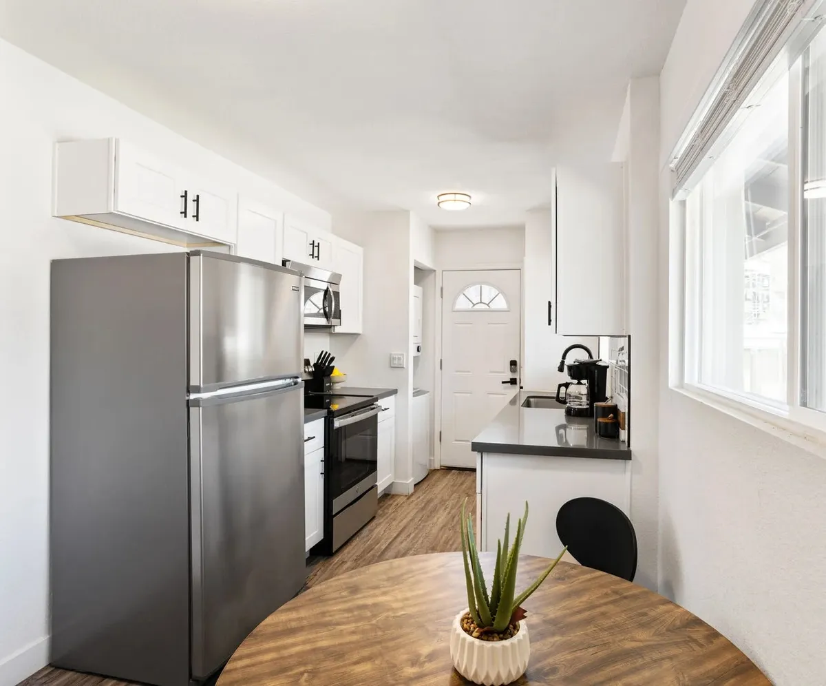 A modern kitchen setup showcases a stainless steel refrigerator and stove, complemented by a dining table adorned with a fresh plant centerpiece. The space feels airy and welcoming, ideal for cooking, sharing recipes, and socializing.