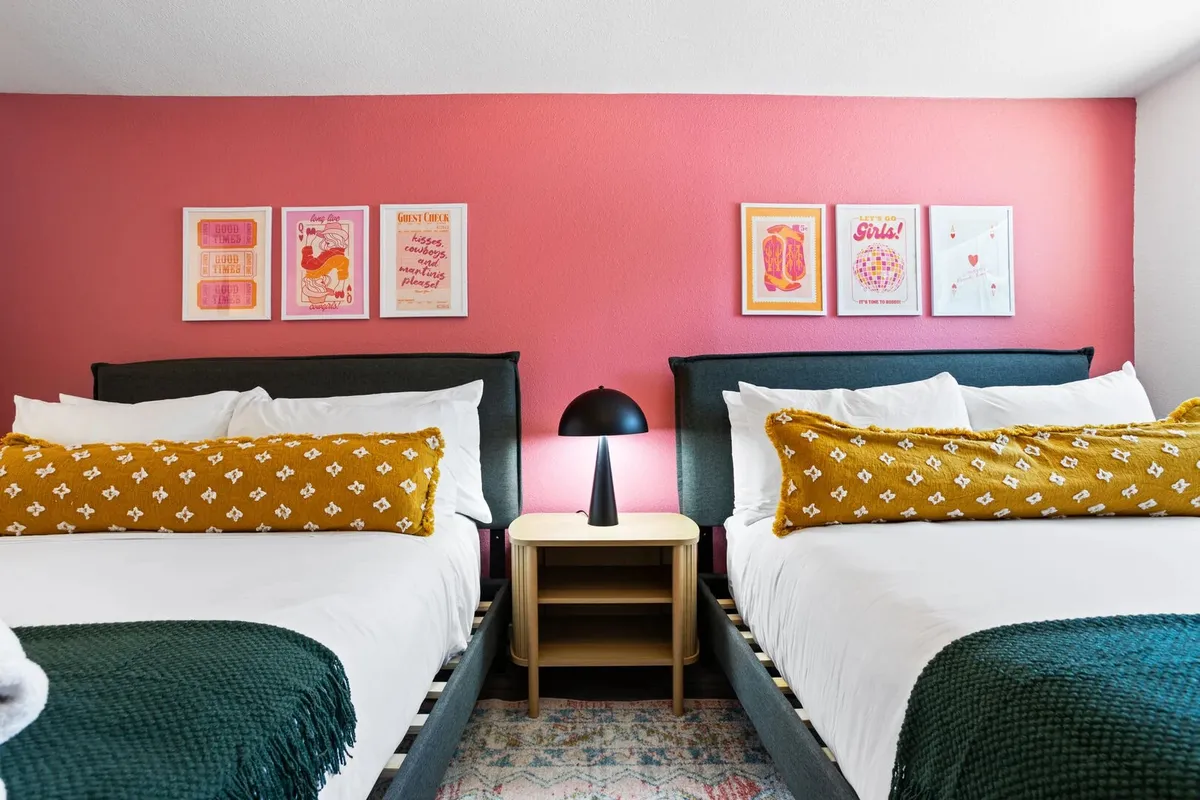 A playful and cozy secondary bedroom with two beds adorned with decorative pillows, vibrant wall art, and a modern bedside lamp. The room is designed for comfort and flexibility, ideal for families or groups of friends.